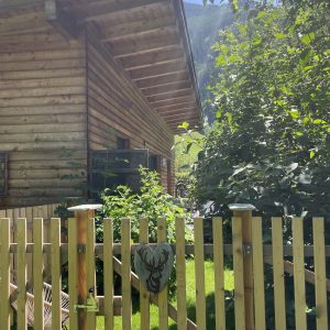 Terrassenbereich mit Zaun, Pflanzen und Teilansicht des Holzhauses