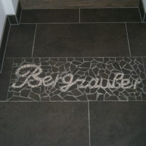 Mosaikfliesen mit Bergzauber-Schriftzug im Eingangsbereich