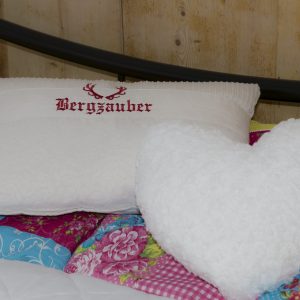 Kissen mit Aufschrift „Bergzauber“ auf gemachtem Bett